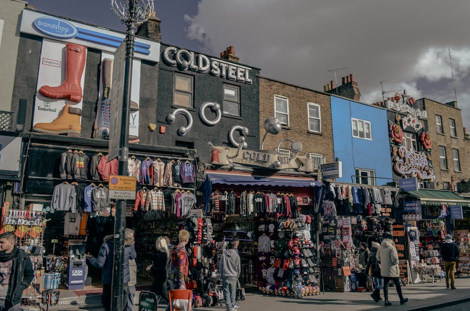 Image depicting a small vendor’s stall at Camden Market with a variety of products including colorful plastic toys, bags, and packaged goods arranged on countertops and shelves. The stall features a